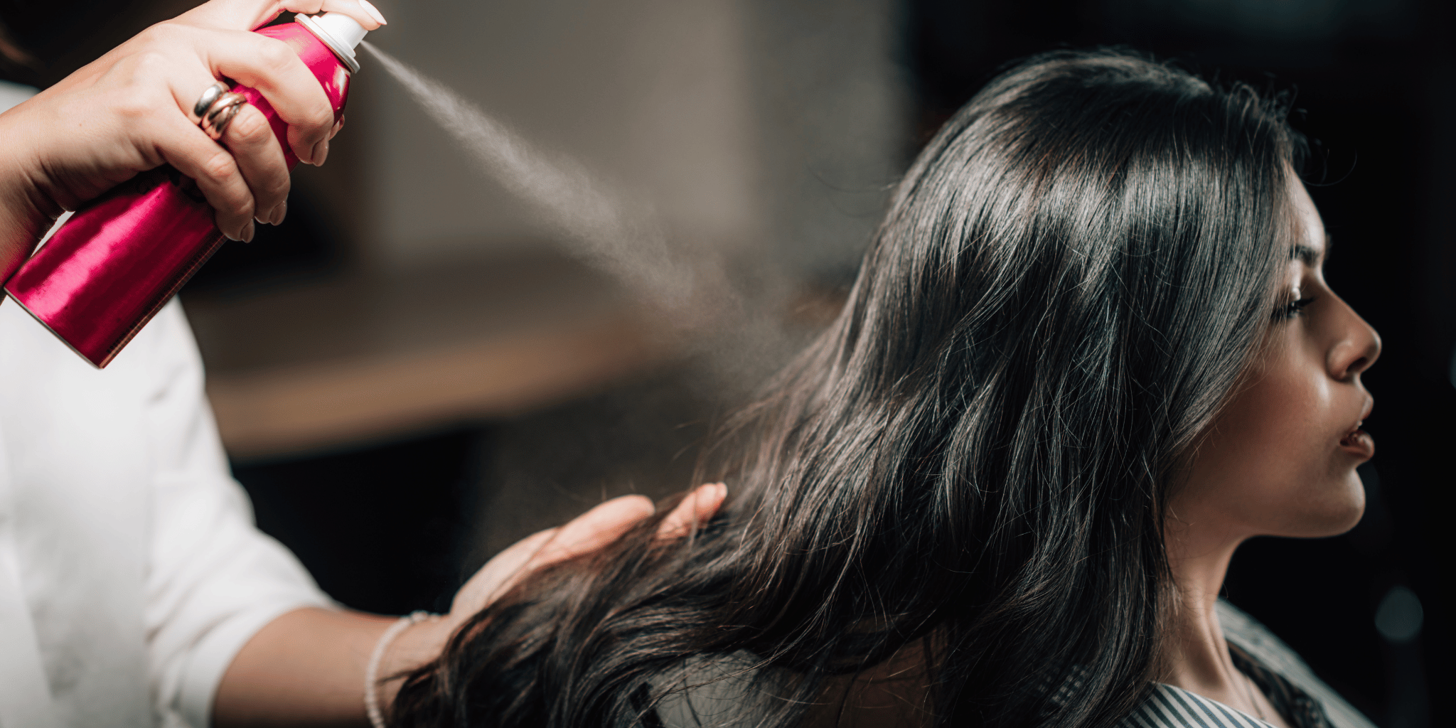 Kvinna med mörkt-hår får sitt hårstylat med hårspray. 