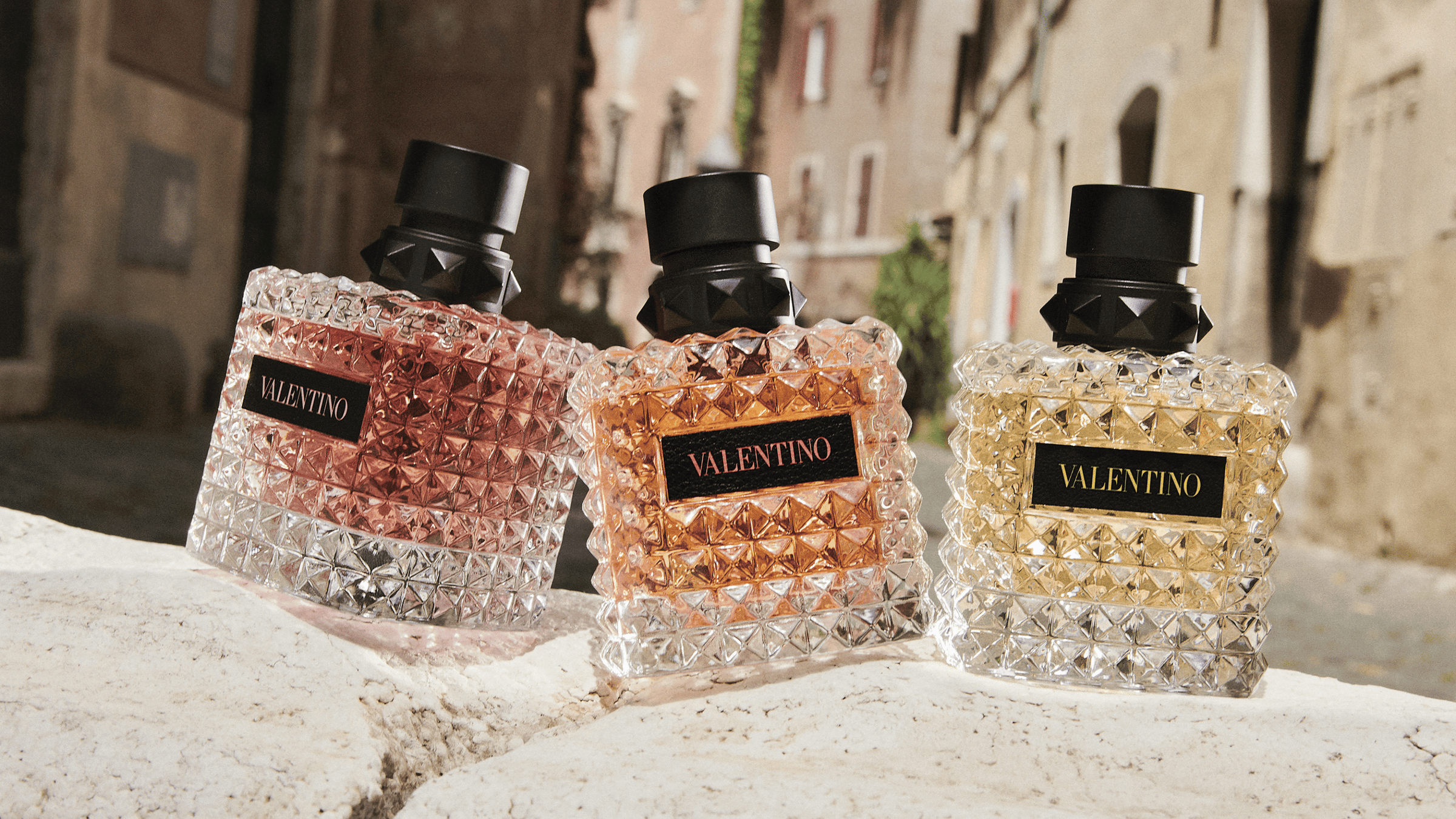 Valentino parfymer som står på en stenmur men hus i bakgrunden. 