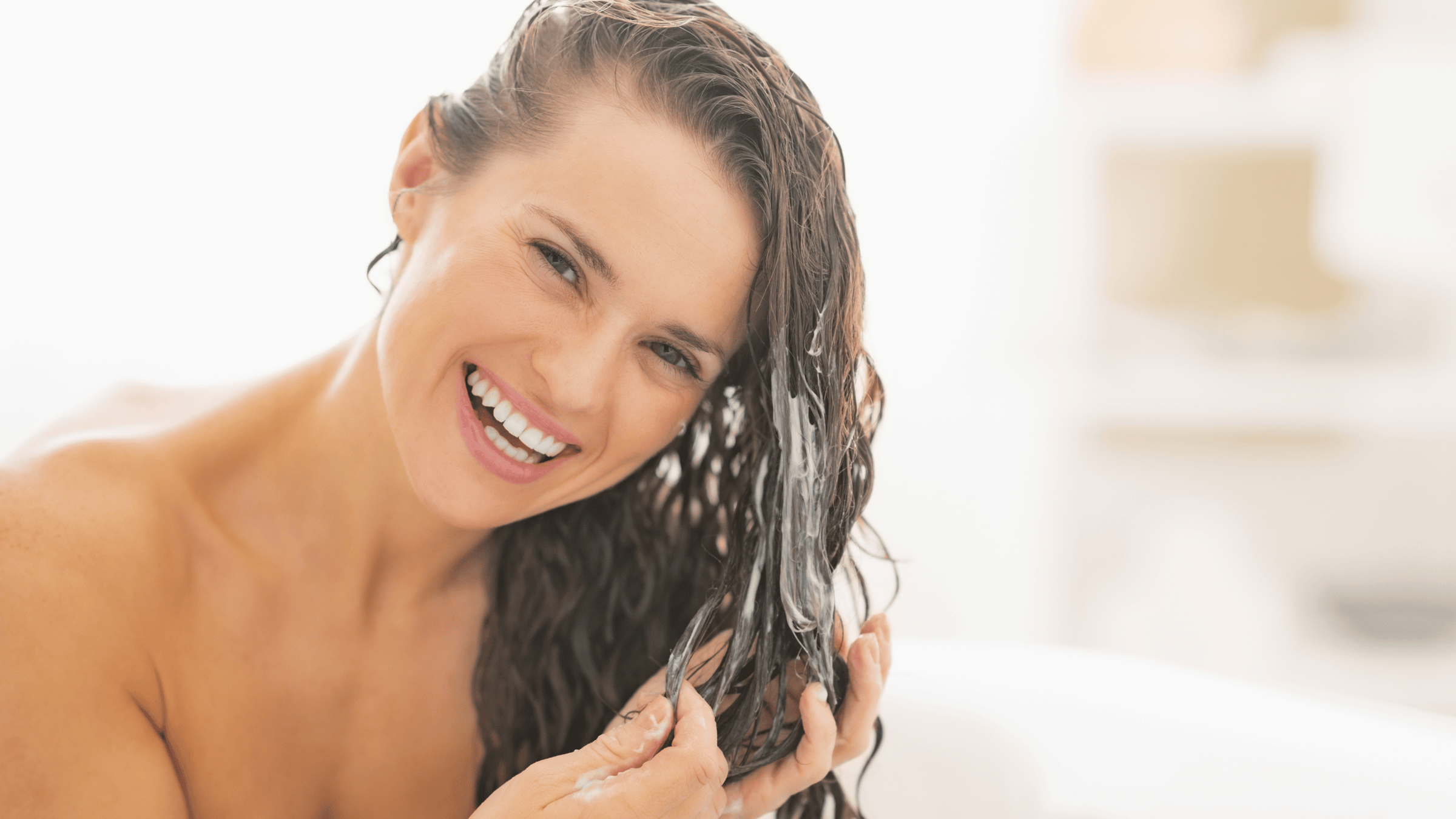 Brunhårig kvinna som balsamerar håret i duschen. 