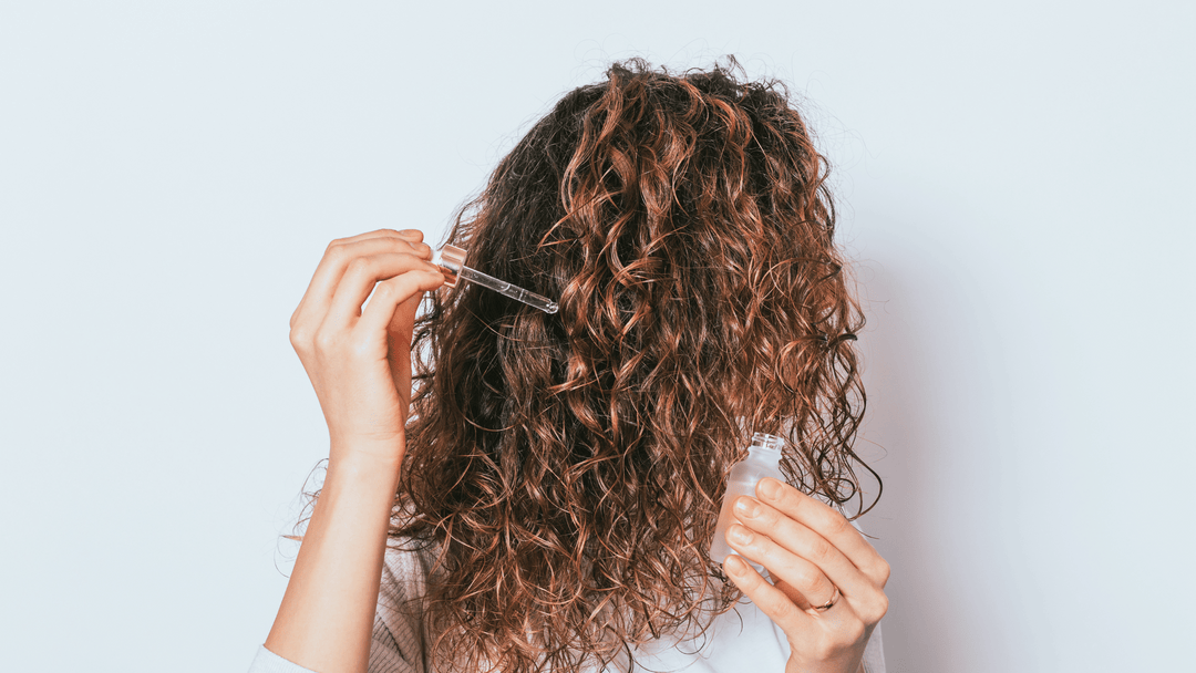 Kvinna med lockigt hår som applicerar hårserum i sitt hår.