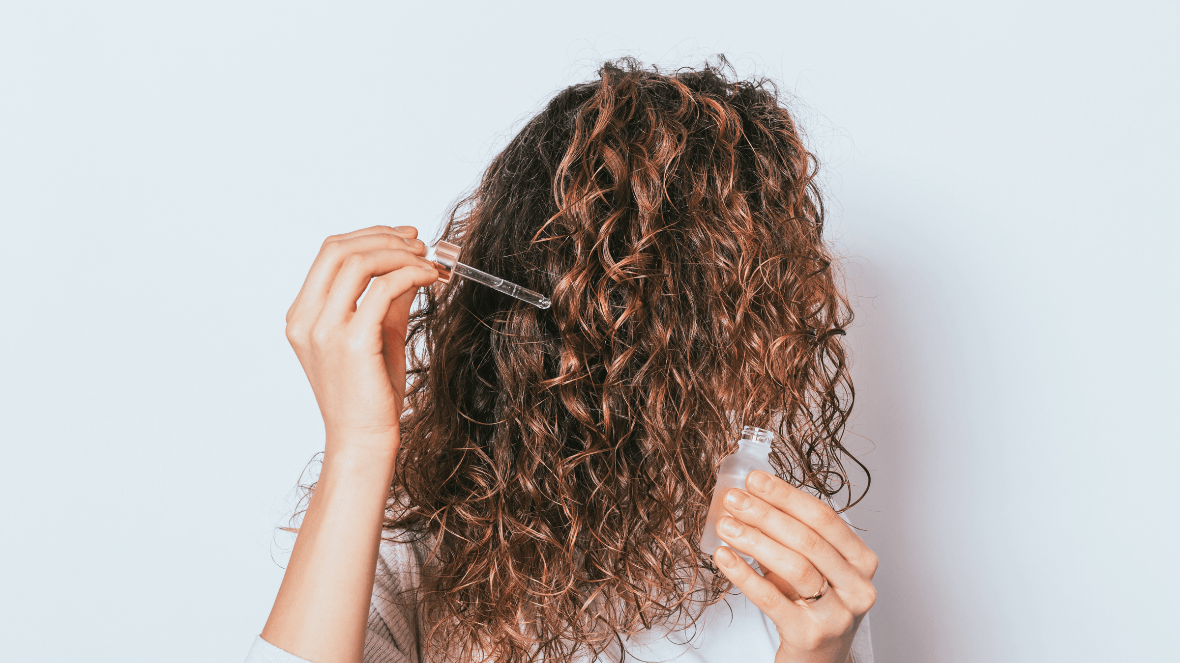 Kvinna med lockigt hår som applicerar hårserum i sitt hår.