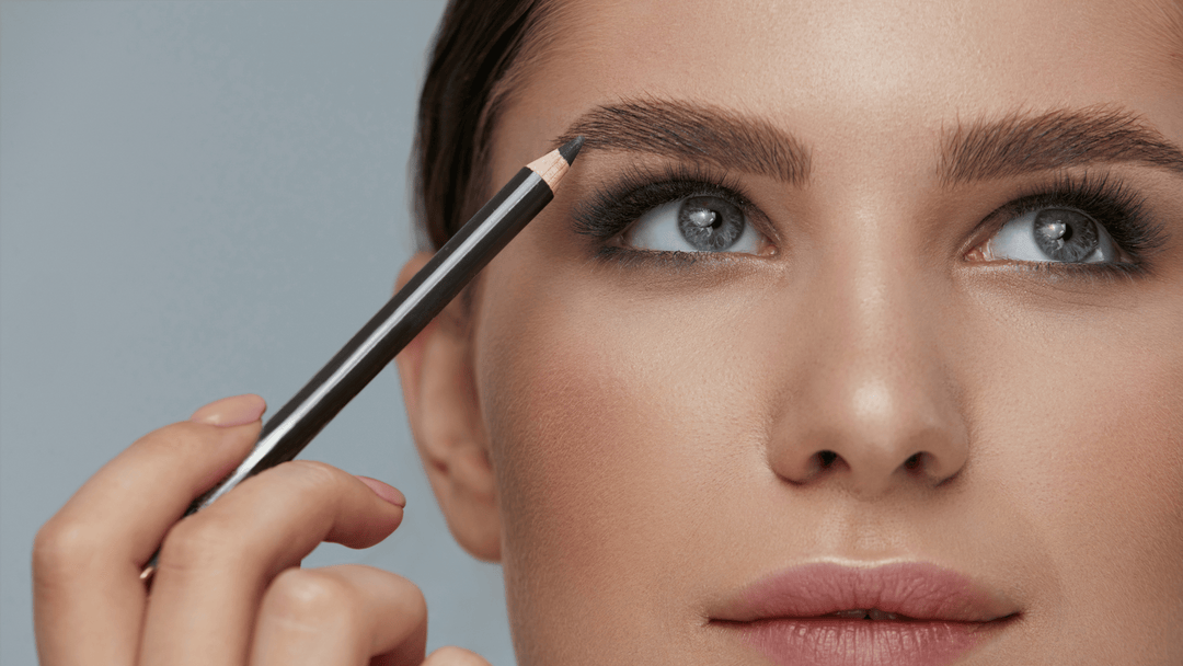 En kvinna använder en ögonbrynspenna för att definiera och fylla i sina ögonbryn, vilket framhäver ögonens intensitet och ger ett polerat utseende.