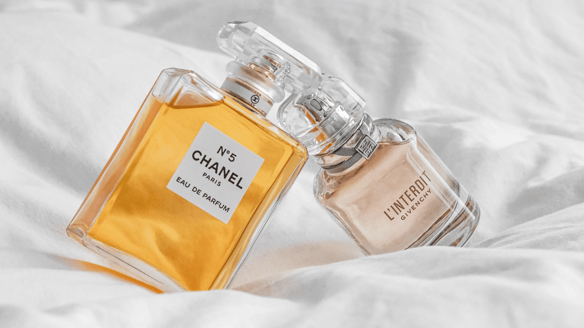 Bild på en parfym från Chanel och en från Givenchy, som ligger i en säng.