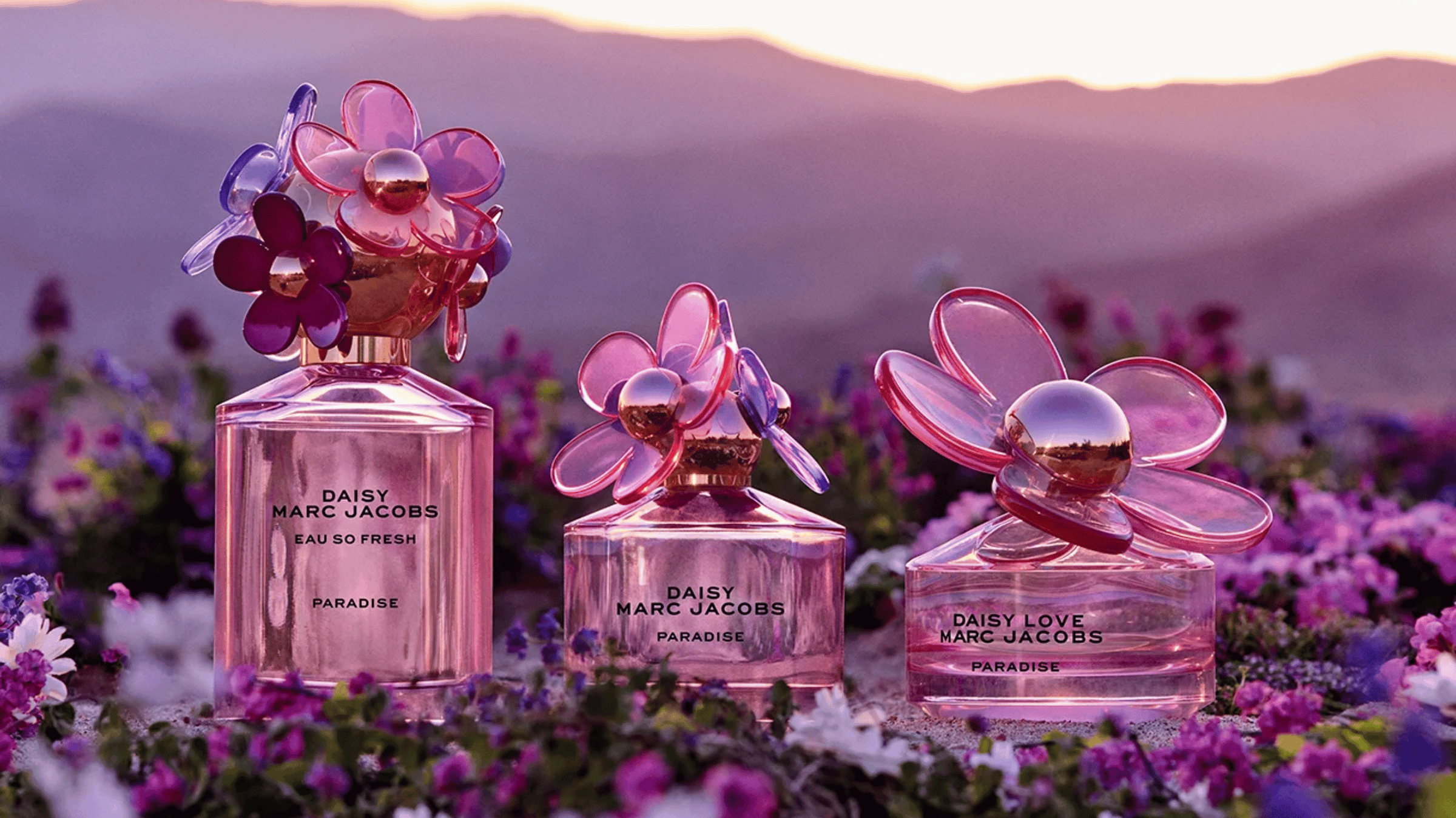 Tre Marc Jacobs parfymer som står på rad med en utsikt av berg i bakgrunden. 